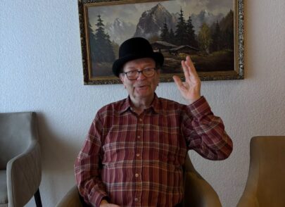 Bewohner mit Hut sitzt am Tisch und hebt seine Hand Bewohner mit Hut sitzt am Tisch und hebt seine Hand